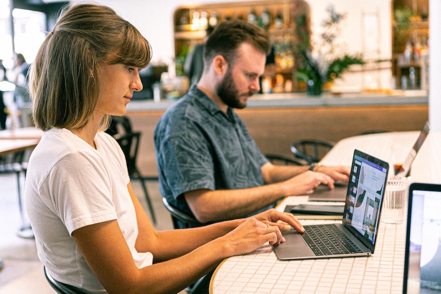 Man and woman working on laptops in a corporate space with many green plants.