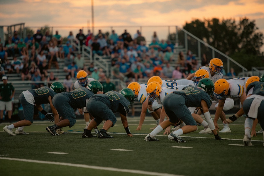 Athletes playing American football with bleacher stands in the background.