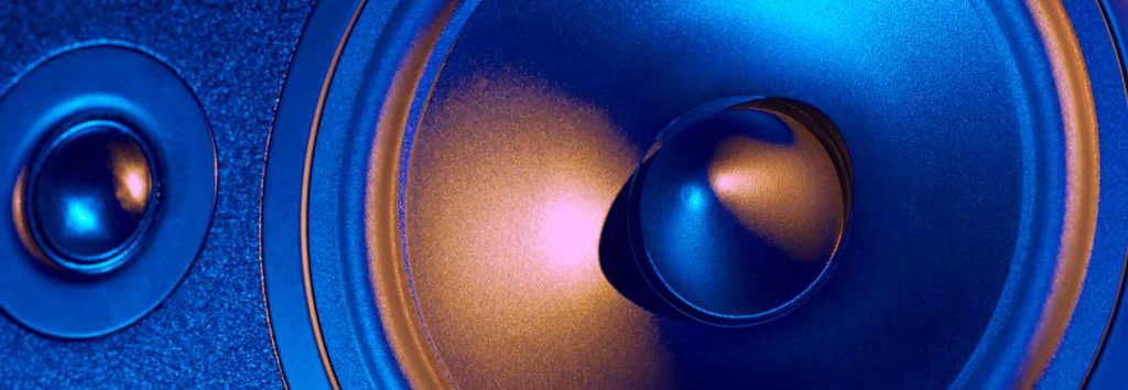 Close-up of two speaker cones in a pro audio system, one large and one small, with a metallic blue and orange hue reflecting light.