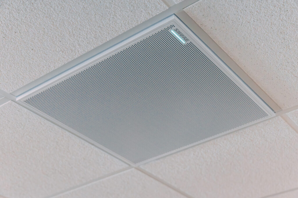 Ceiling-mounted rectangular microphone panel with a grid mesh design installed in a light-colored tiled ceiling. Conference Room Microphone
